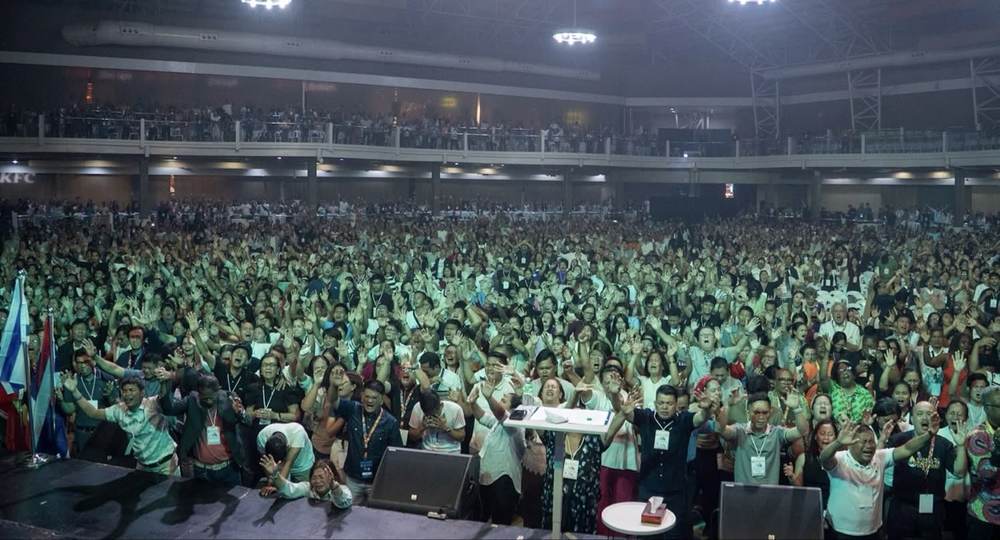 A packed international congregation responding together in prayer